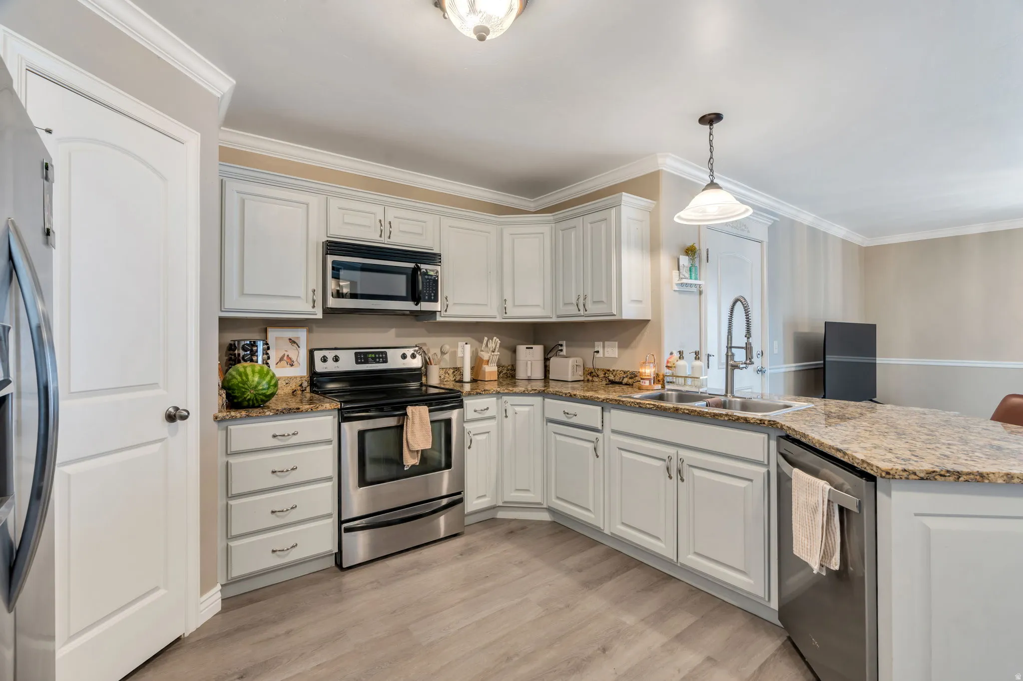 Kitchen with light-toned cabinetry, stainless steel appliances, granite countertops, and wood-finish flooring