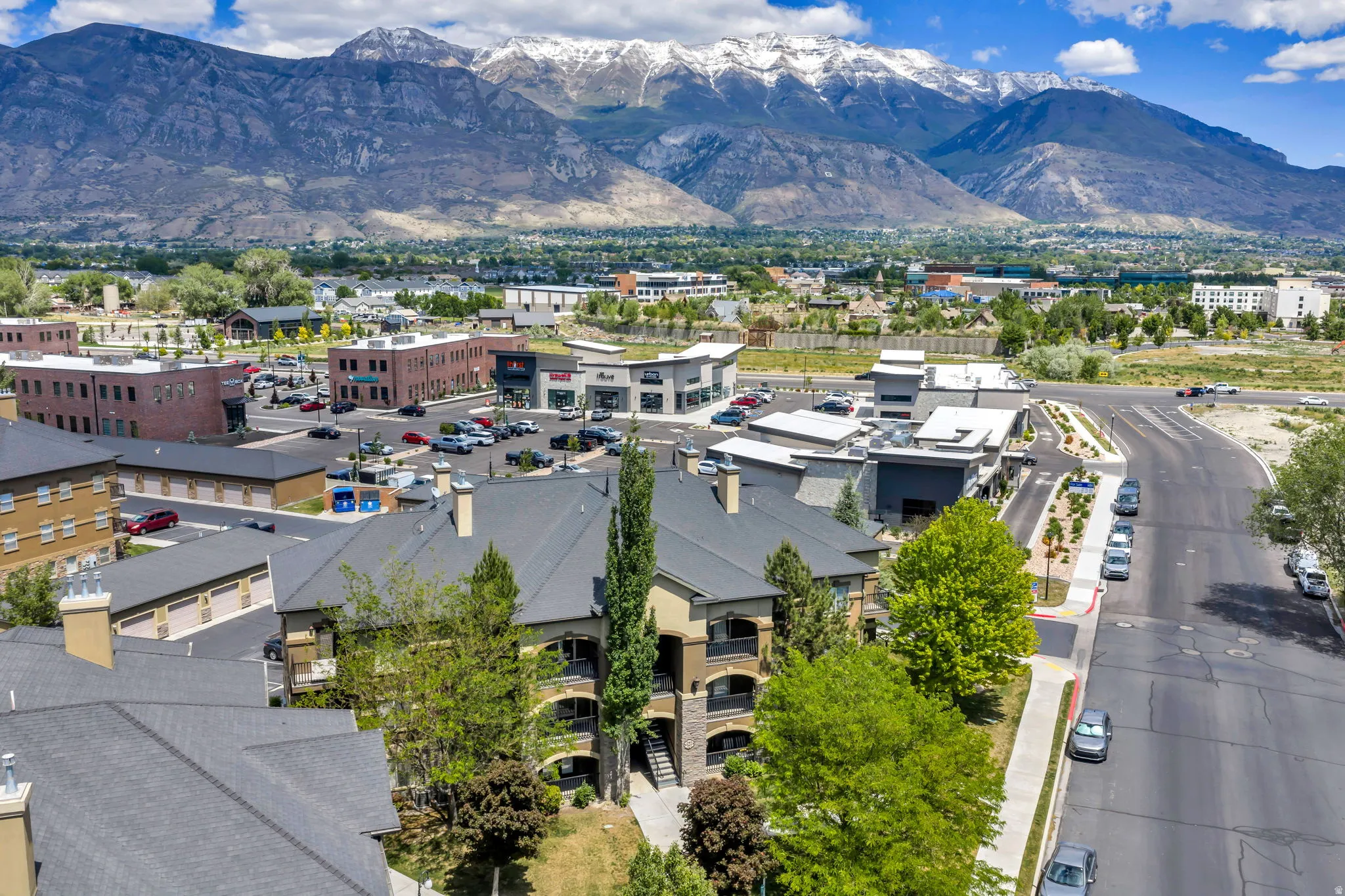 Multi-story residential complex featuring balconies, mature trees, and a mountain backdrop