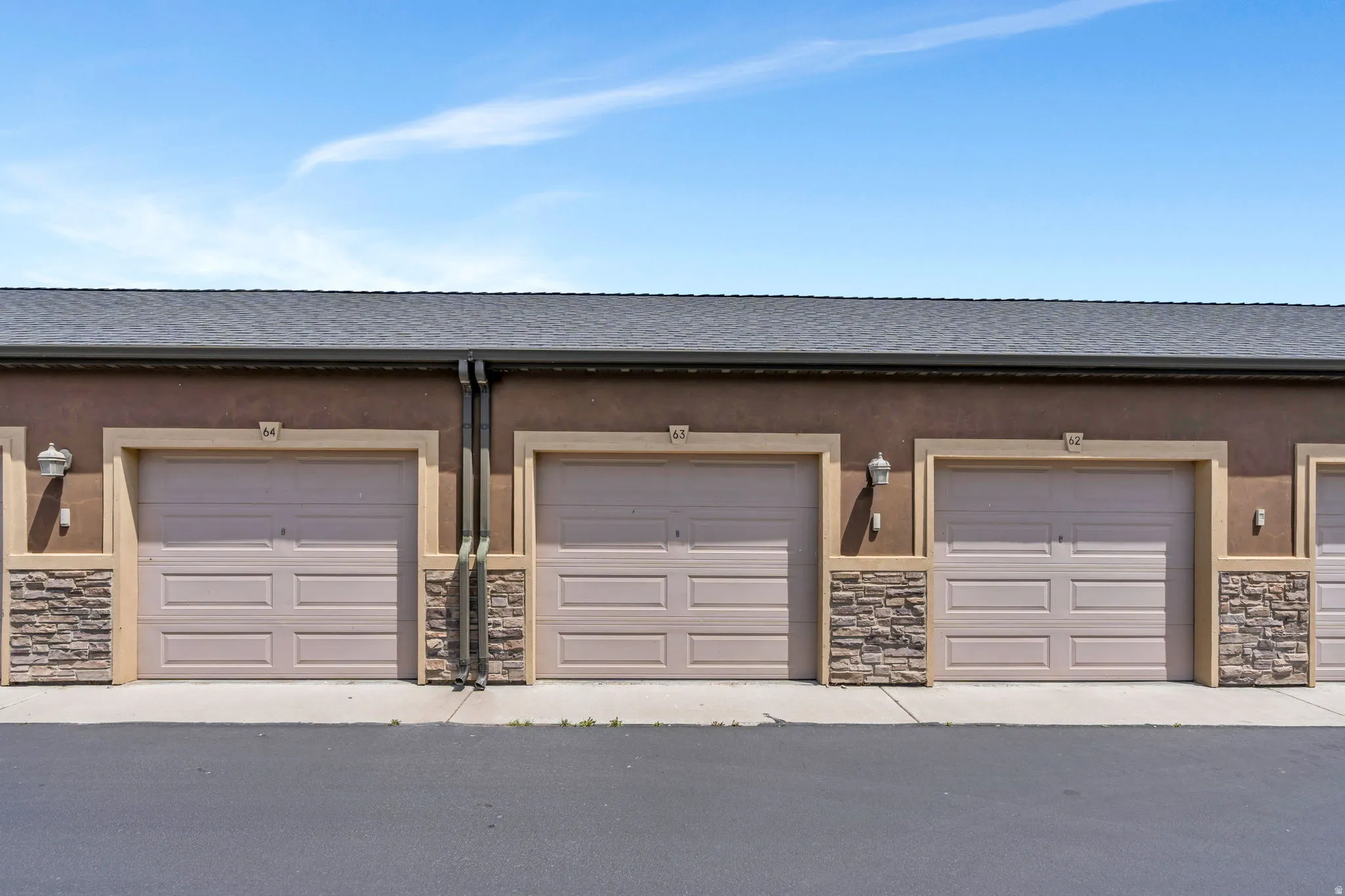 Row of garages featuring tan doors with panel detailing, stone veneer accents, and exterior lighting fixtures