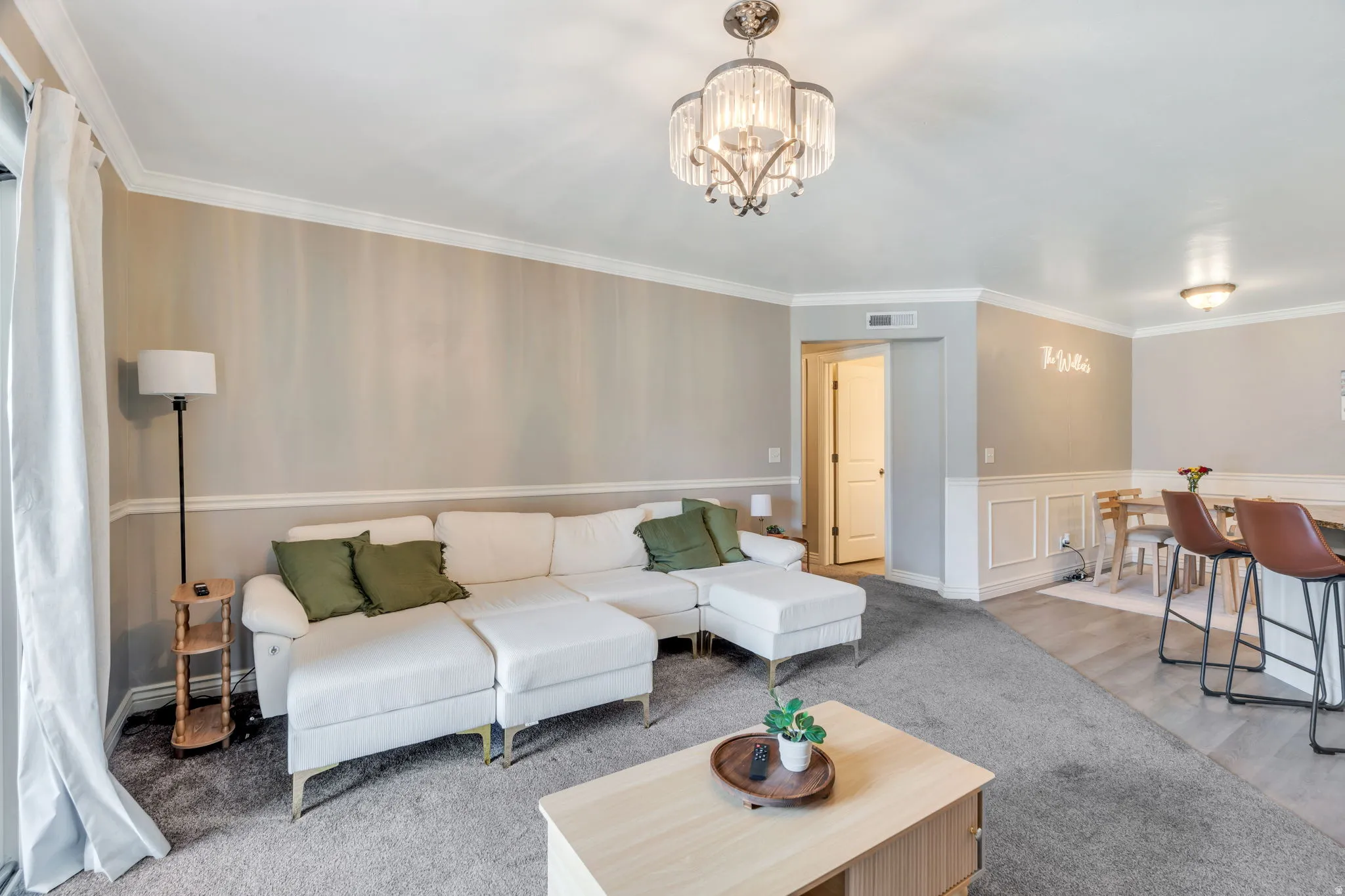 Living area featuring a crystal chandelier, crown molding, two-tone wall treatment with wainscoting, and a doorway leading to an interior room