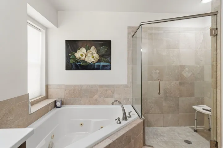 Spa-like bathroom with a corner jetted soaking tub, a separate glass-enclosed shower with tiled walls and floor, brushed nickel fixtures, and neutral tile surround