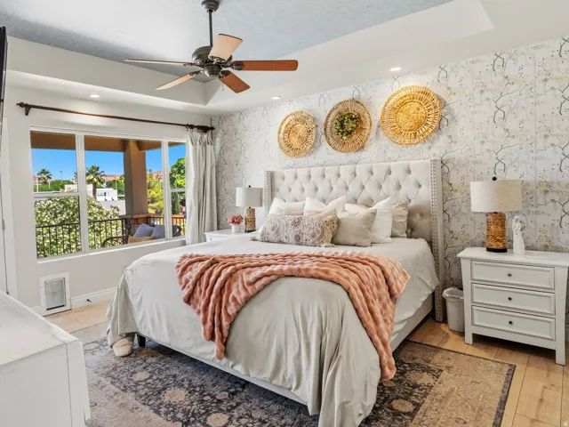 Spacious bedroom featuring wood-finish flooring, a tray ceiling with recessed lighting, an overhead ceiling fan, and a large window overlooking an exterior balcony