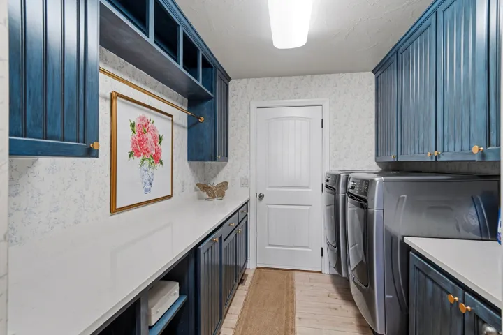 Dedicated laundry space featuring a side-by-side washer and dryer set, extensive blue-toned cabinetry, long white countertops, and open shelving