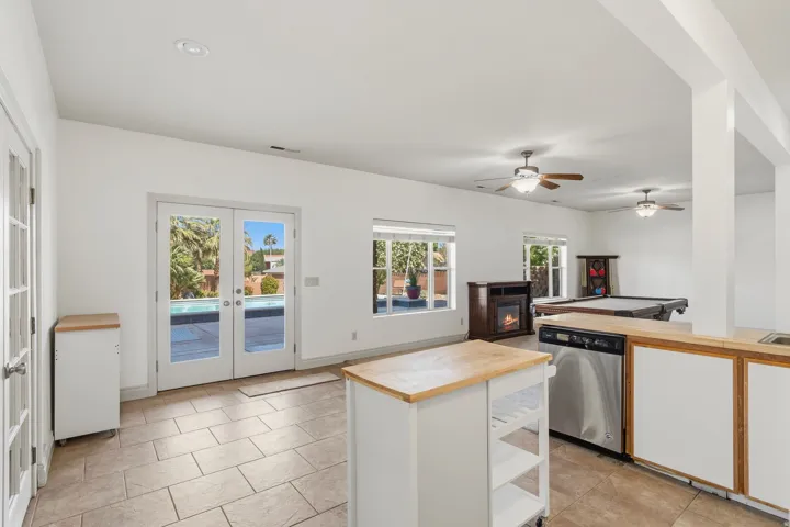 Spacious interior featuring tile flooring, French doors opening to an outdoor pool area, multiple ceiling fans, and a built-in wet bar with stainless steel appliances
