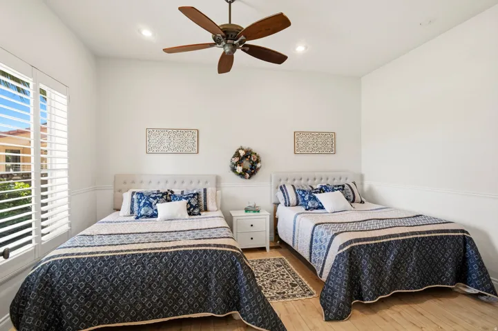 Bright room featuring two upholstered headboards, a ceiling fan with integrated lighting, recessed lighting, wood-finish flooring, and a window with white plantation shutters