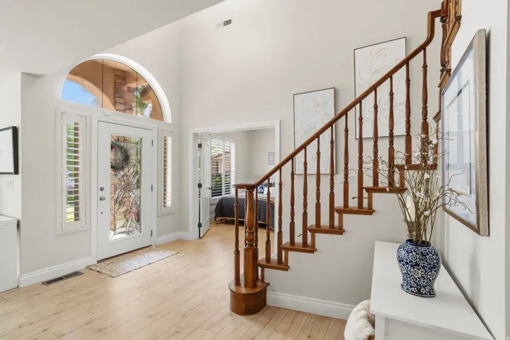 Foyer featuring a grand staircase with wood balusters, light wood-finish flooring, a white entry door with decorative glass, sidelights with plantation shutters, and an arched transom window