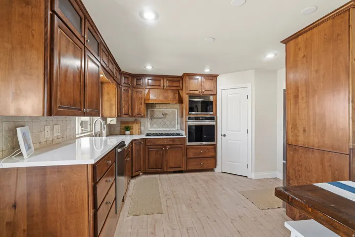 Spacious kitchen featuring extensive wood cabinetry, light-toned wood-finish flooring, white countertops, stainless steel appliances, and recessed lighting