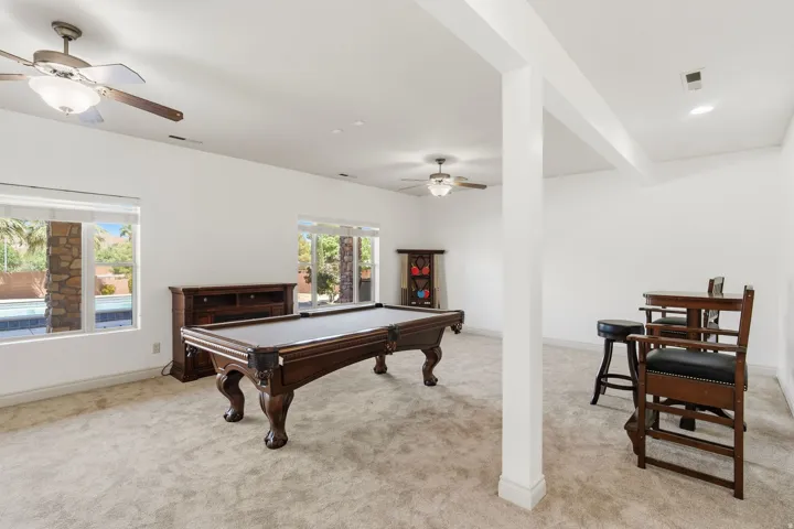 Spacious entertainment area featuring neutral-toned carpeting, two ceiling fans, and multiple windows