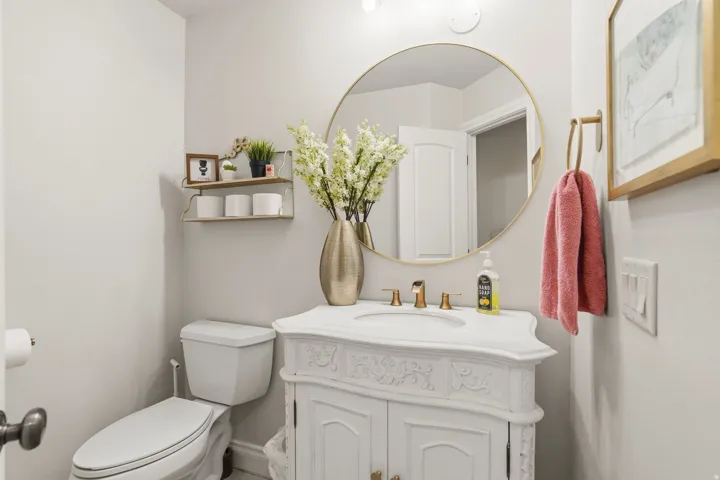 Bathroom vanity featuring a vessel sink with a gold-finish faucet, a large round gold-framed mirror, and a white carved cabinet