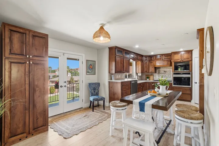Kitchen featuring rich wood cabinetry, stainless steel appliances, light-toned wood-finish flooring, a central island with seating, and double french doors opening to a balcony