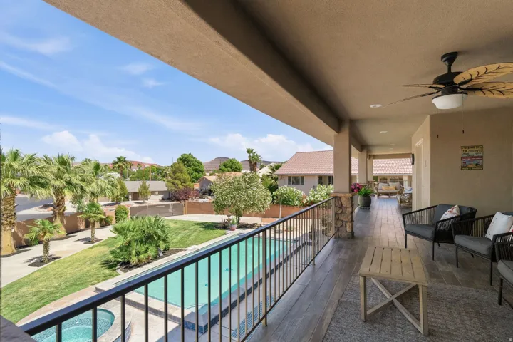 Upper-level covered patio featuring a leaf-bladed ceiling fan, recessed lighting, and stone-clad pillars