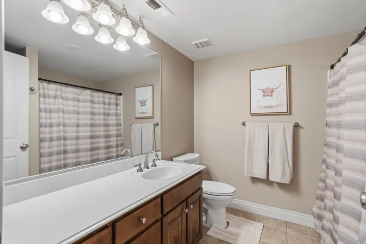 Bathroom featuring a wood-finish vanity with a white countertop and integrated sink, a large wall-mounted mirror, and tile flooring