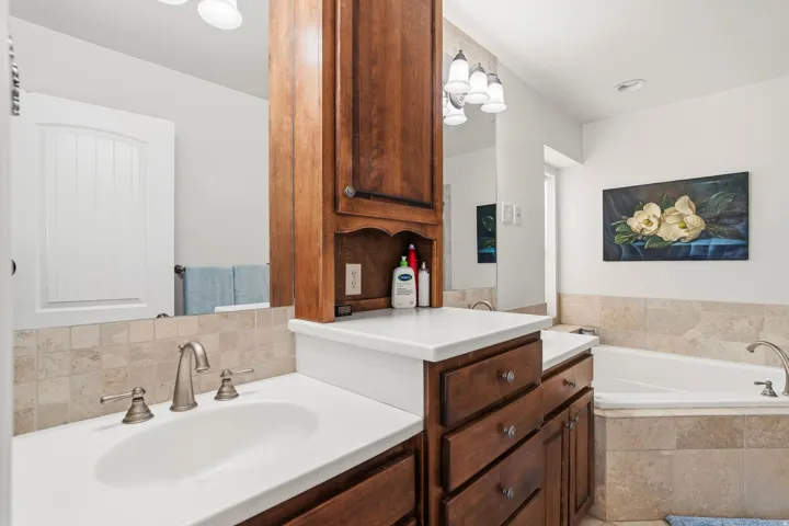 Bathroom vanity featuring a built-in wood-finish storage cabinet, dual sinks, and an integrated soaking tub
