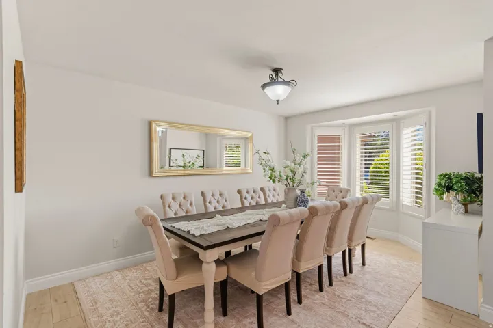 Dining area featuring light wood-finish flooring, a contemporary ceiling light fixture, and a bay window with plantation shutters