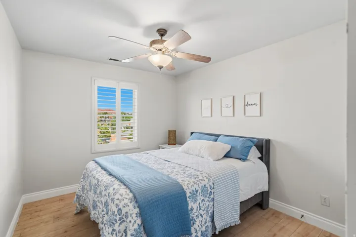 Bedroom featuring wood-finish flooring, white baseboards, a window with white plantation shutters, and a ceiling fan with integrated lighting
