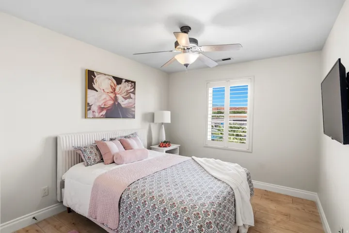 Bedroom featuring wood-finish flooring, white baseboards, a ceiling fan with light fixture, and a window with white plantation shutters
