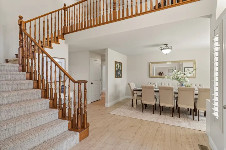 Foyer featuring a grand staircase with wood banister and balusters, textured carpeted treads, and wood-finish flooring extending into the dining area