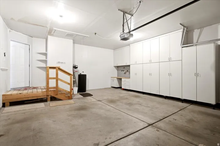 Integrated garage featuring extensive white cabinetry, a built-in workbench, an automatic garage door opener, a wooden entry platform with railing, and a side access door