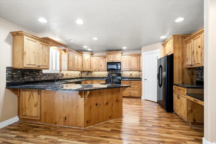 Spacious kitchen featuring extensive wood cabinetry, dark countertops, a large central island, black appliances, and wood-finish flooring