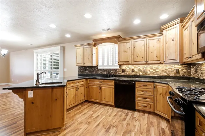 Spacious kitchen featuring a large island with a sink, light wood cabinetry, dark countertops, a tiled backsplash, and recessed lighting