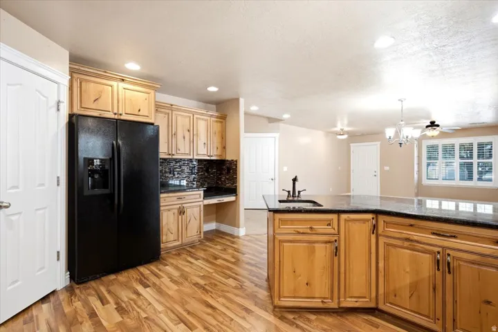 Kitchen featuring natural wood cabinetry, dark countertops, wood-finish flooring, a mosaic tile backsplash, and recessed lighting