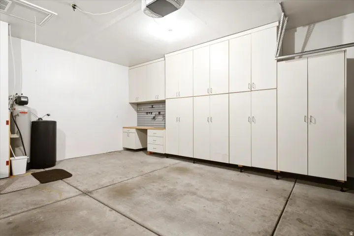 Garage featuring extensive built-in white cabinetry, workbench with light wood-finish countertop, organized pegboard, and utility sink