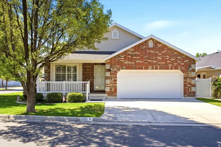 Brick and stucco exterior featuring a two-car garage, covered porch with white railing, and a manicured lawn