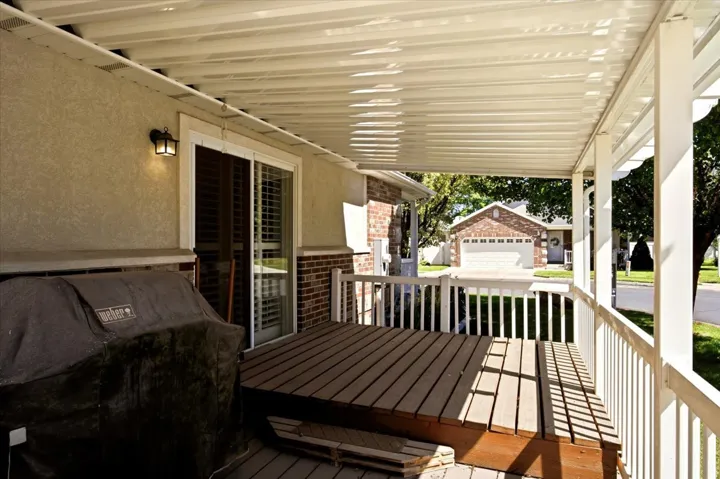 Covered patio featuring a wood-finish deck with white railing, stucco exterior, and a sliding glass door