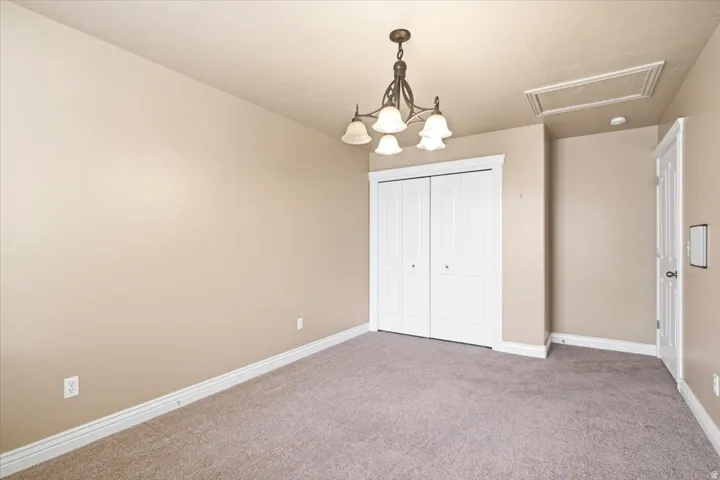 Carpeted room featuring a ceiling-mounted chandelier, white bi-fold closet doors, white baseboards, and a white interior door