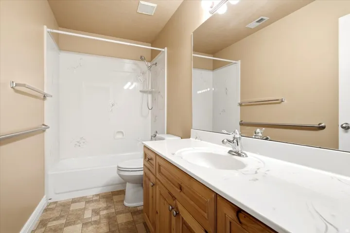 Bathroom featuring a white bathtub and shower surround, a wood-finish vanity with a white countertop and integrated sink, a chrome faucet, and patterned floor tile
