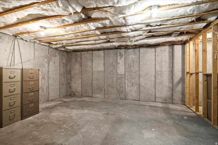 Unfinished basement space featuring exposed ceiling joists with insulation, concrete slab flooring, and concrete foundation walls