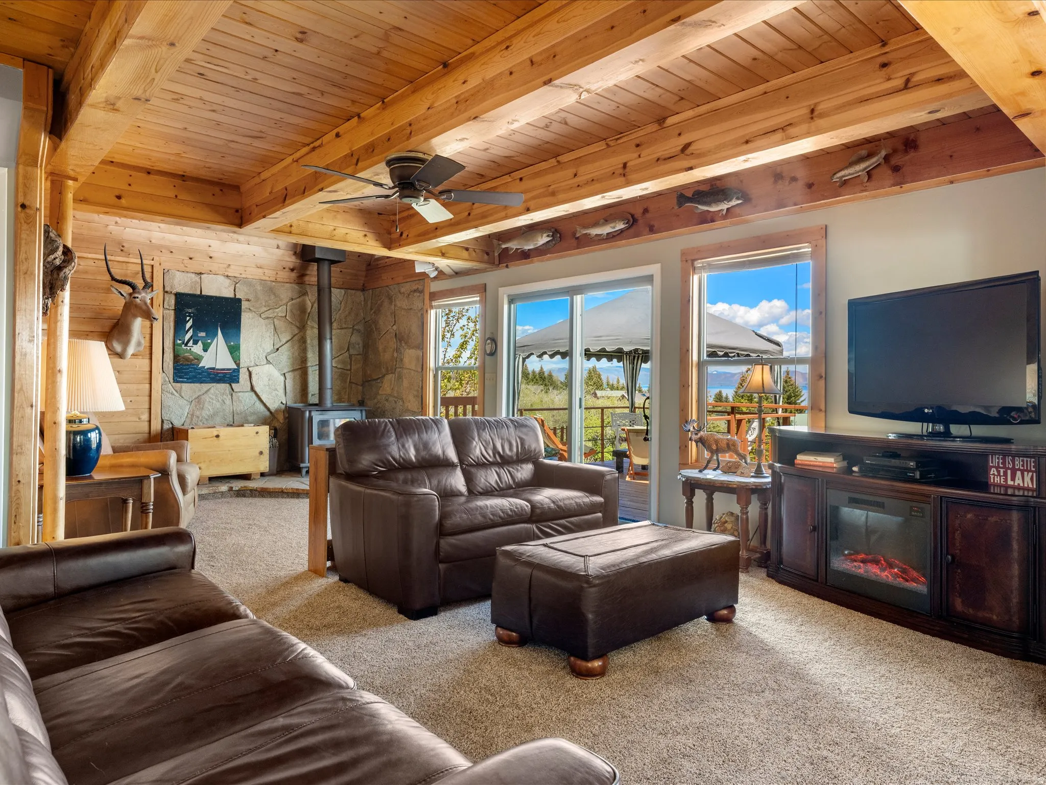 Living area featuring a wood-planked ceiling with exposed beams, a built-in stone accent wall with a wood-burning stove, and carpeted flooring