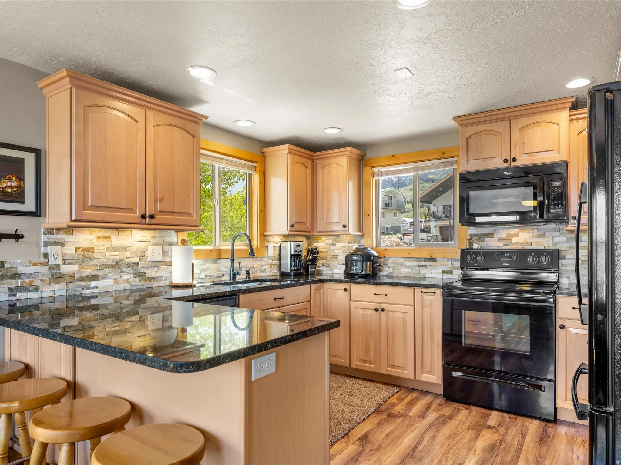 Kitchen featuring wood-finish flooring, natural wood cabinetry, dark stone countertops, a mosaic tile backsplash.