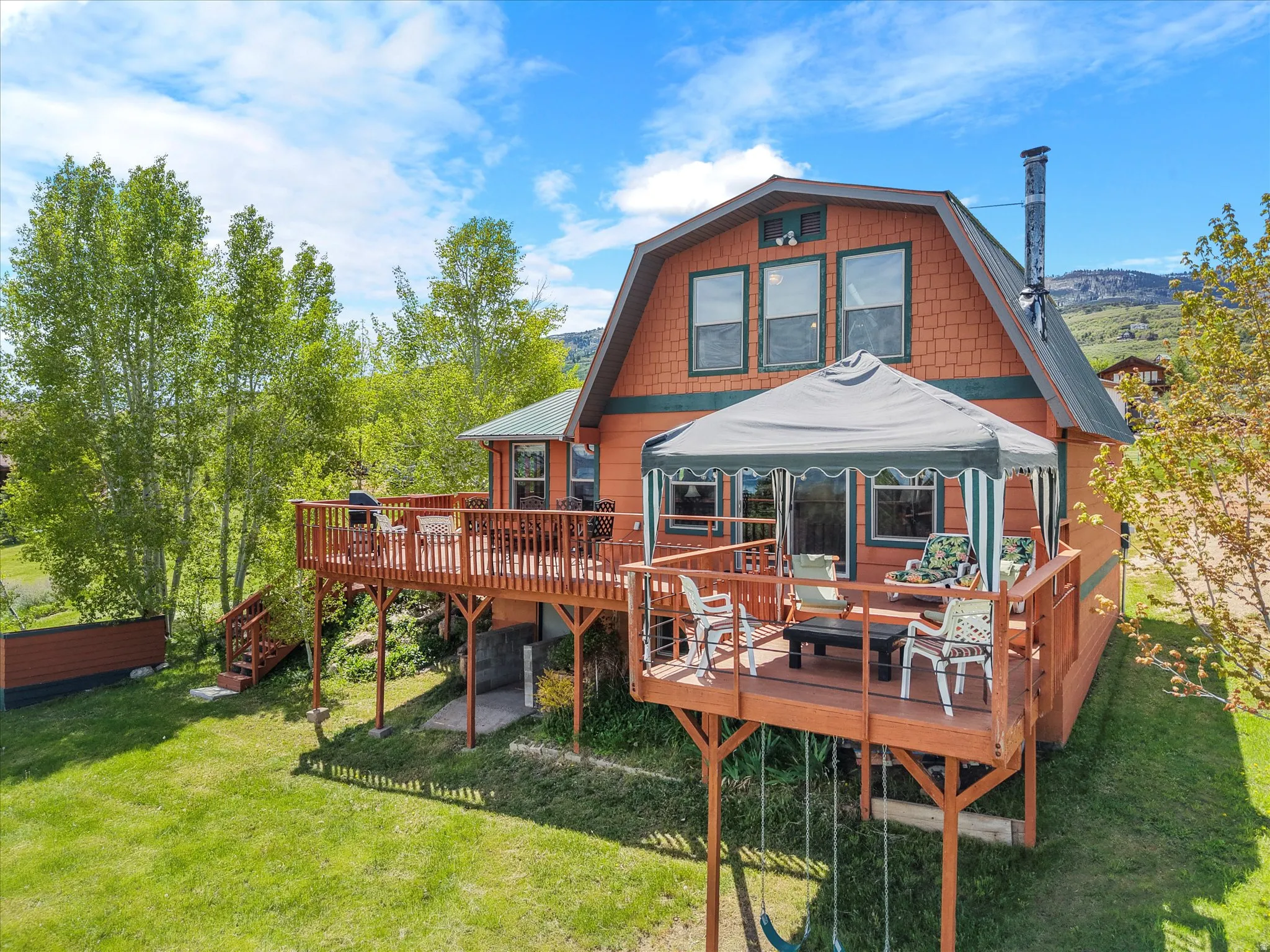 Two-story gambrel-roof residence featuring an expansive wooden deck with a covered outdoor area