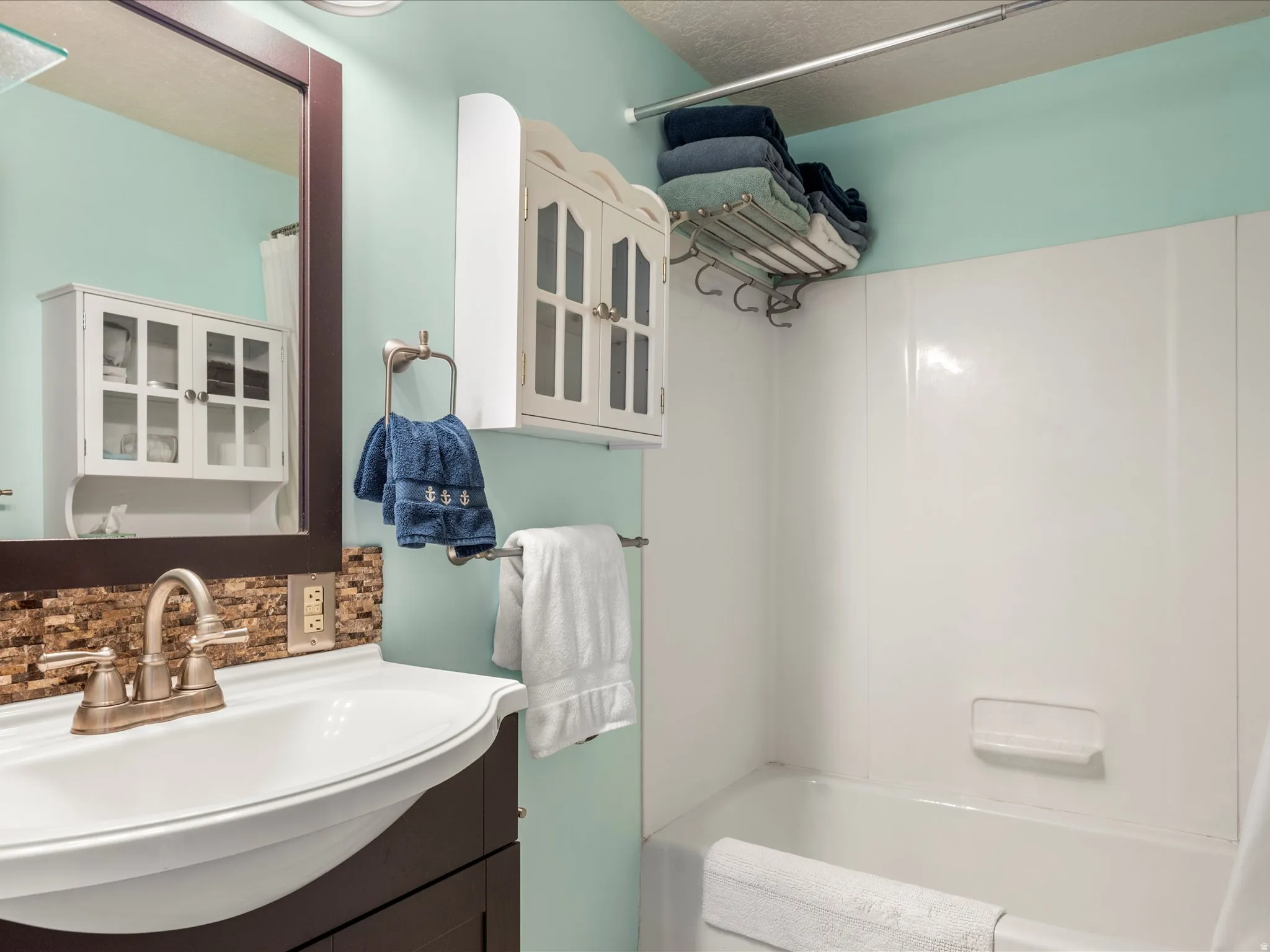 Bathroom featuring a white drop-in sink, a two-handle brushed nickel faucet, and a stone-look tile backsplash