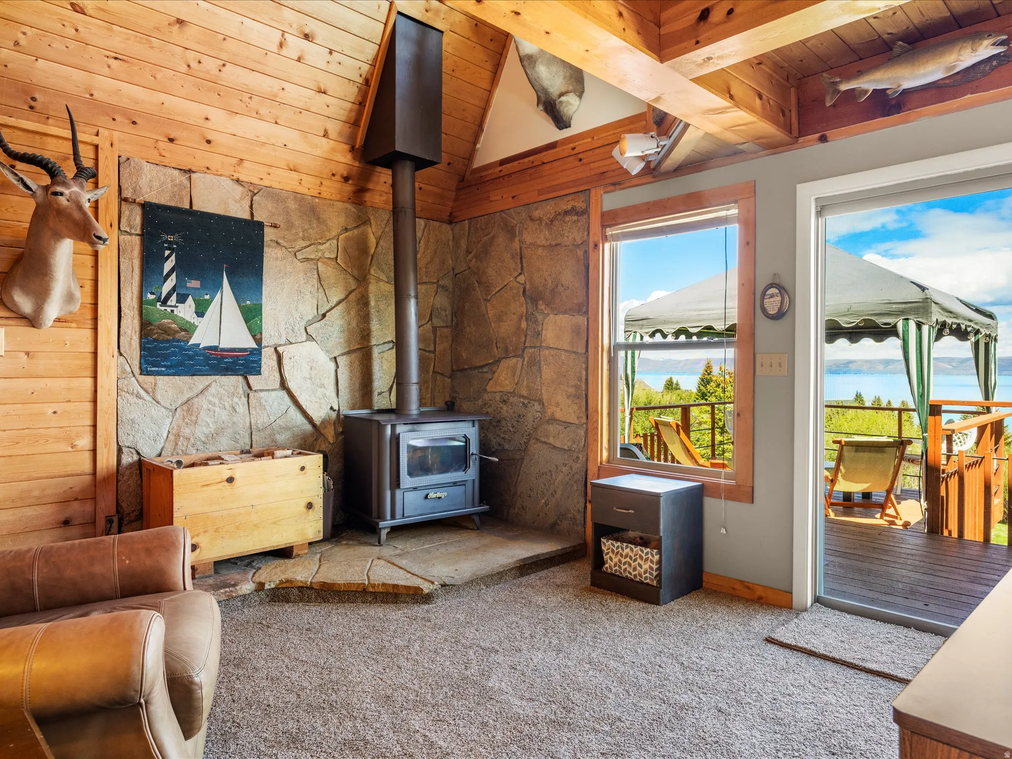 Living area featuring a stone accent wall, a freestanding wood-burning stove, wood plank wall paneling, and an exposed wood beam ceiling