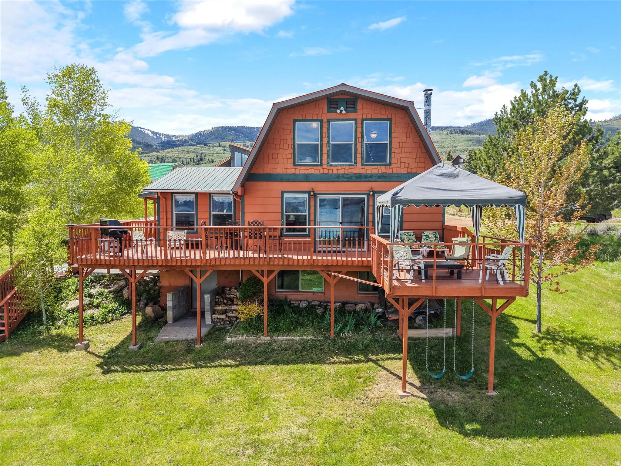 Gambrel-style home featuring an expansive wood deck, multiple large windows, and a covered outdoor dining area