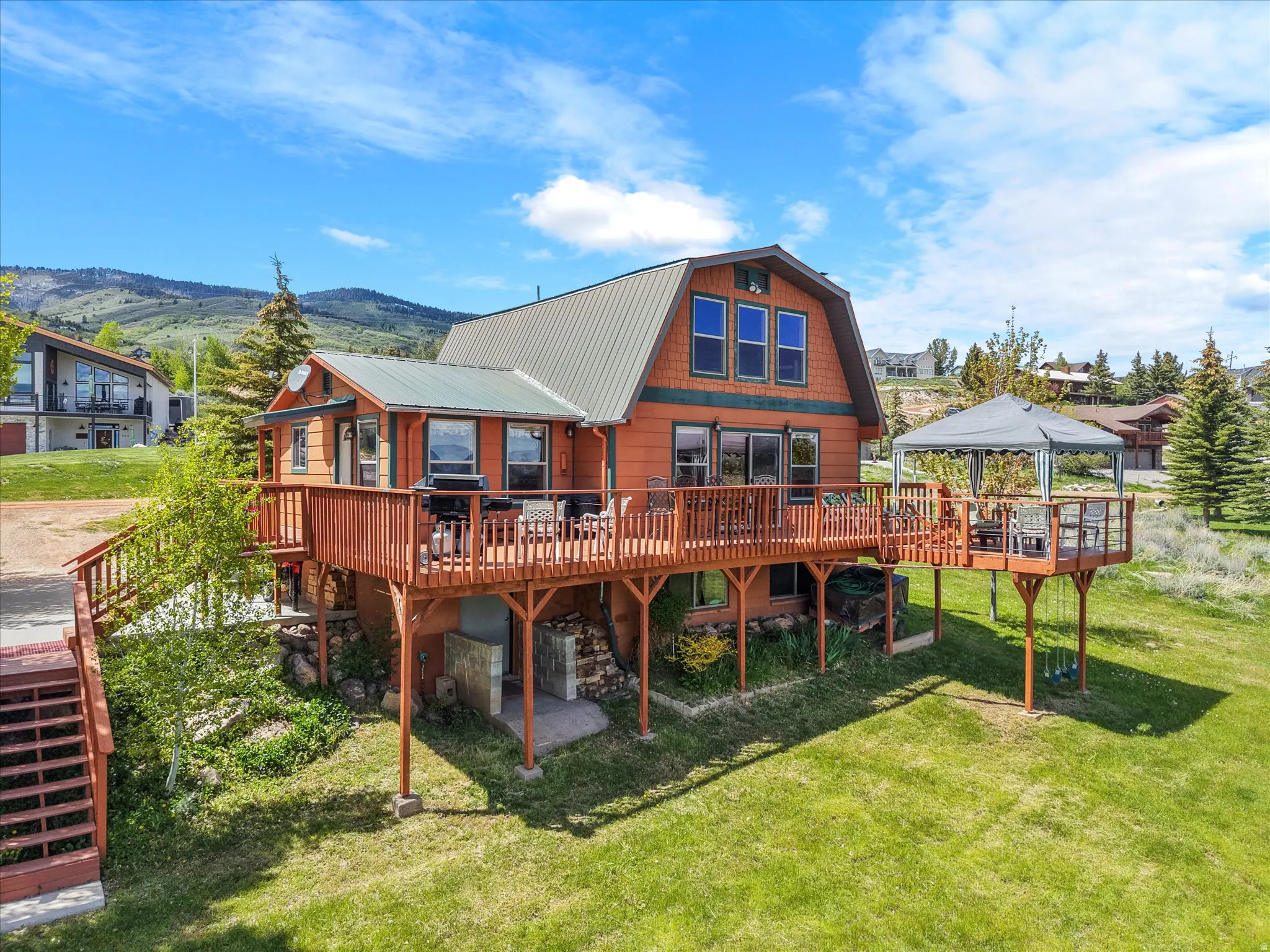 Wood-sided residence featuring a gambrel roof and extensive wrap-around decking
