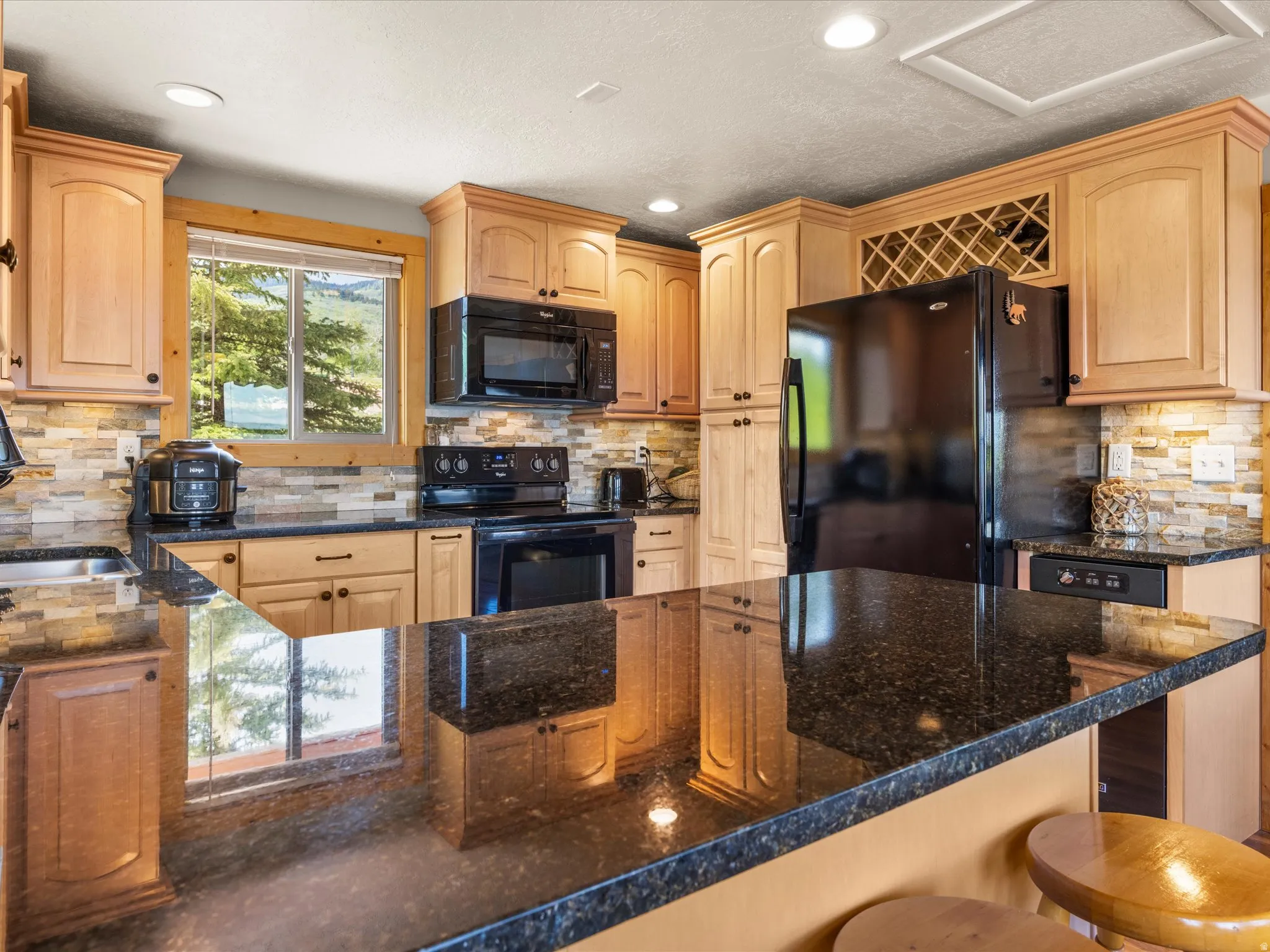 Kitchen featuring granite countertops, light wood-finish cabinetry, a stone-finish backsplash, and an integrated wine rack