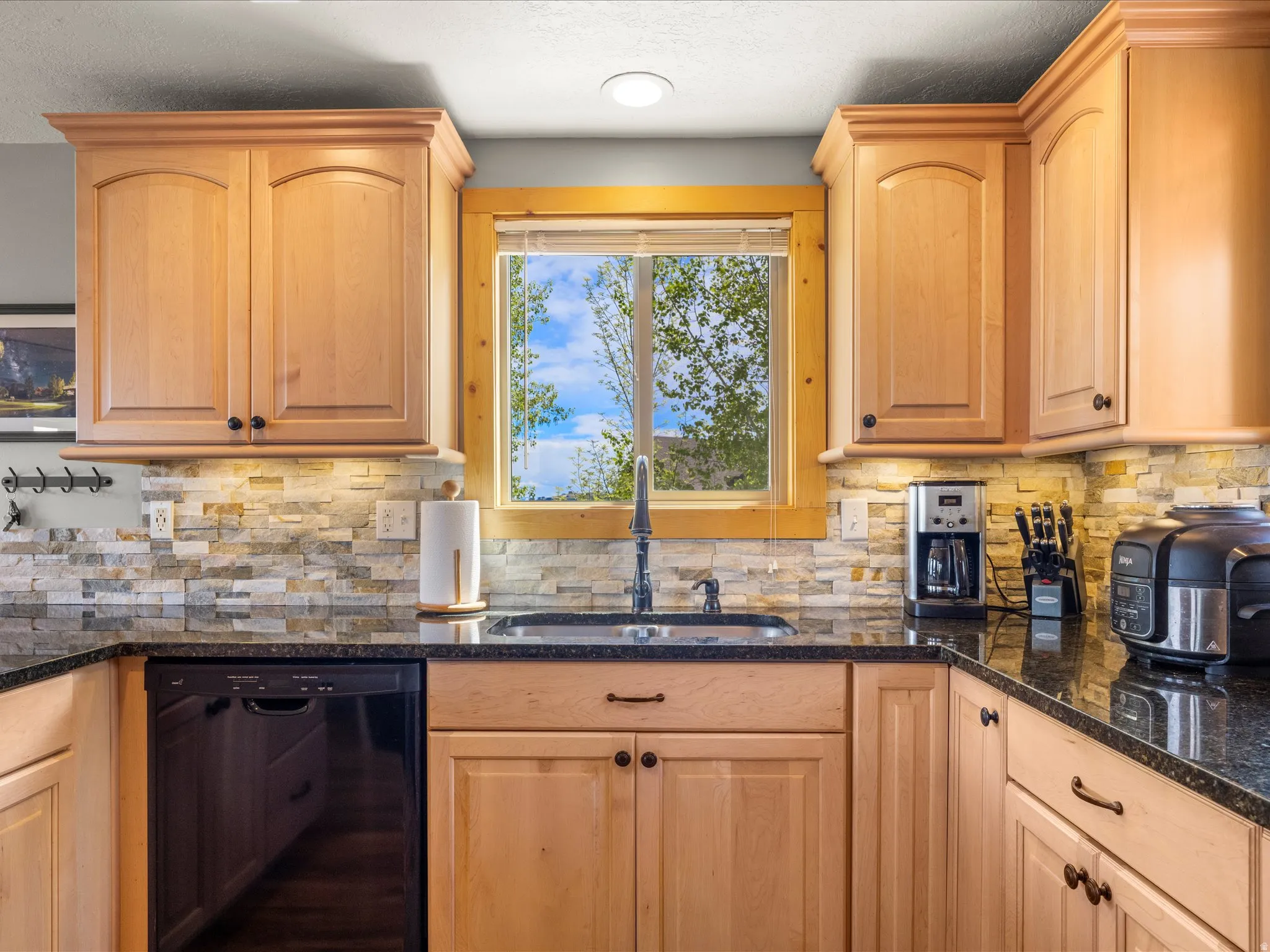 Kitchen featuring light wood cabinetry with arch panel doors and dark hardware, granite countertops, and a stacked stone backsplash