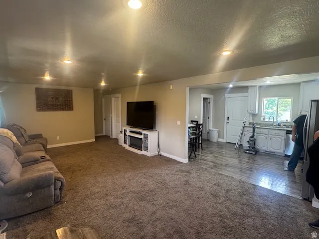 Open concept living area featuring recessed lighting, a built-in media console, wood-finish flooring, and a kitchen with white cabinetry and a window over the sink