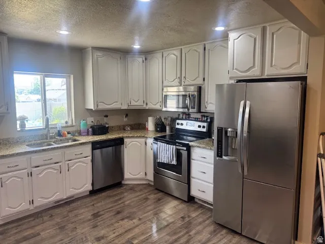 Kitchen featuring white cabinetry, wood-finish flooring, recessed lighting, and stainless steel appliances including a side-by-side refrigerator, microwave, and range
