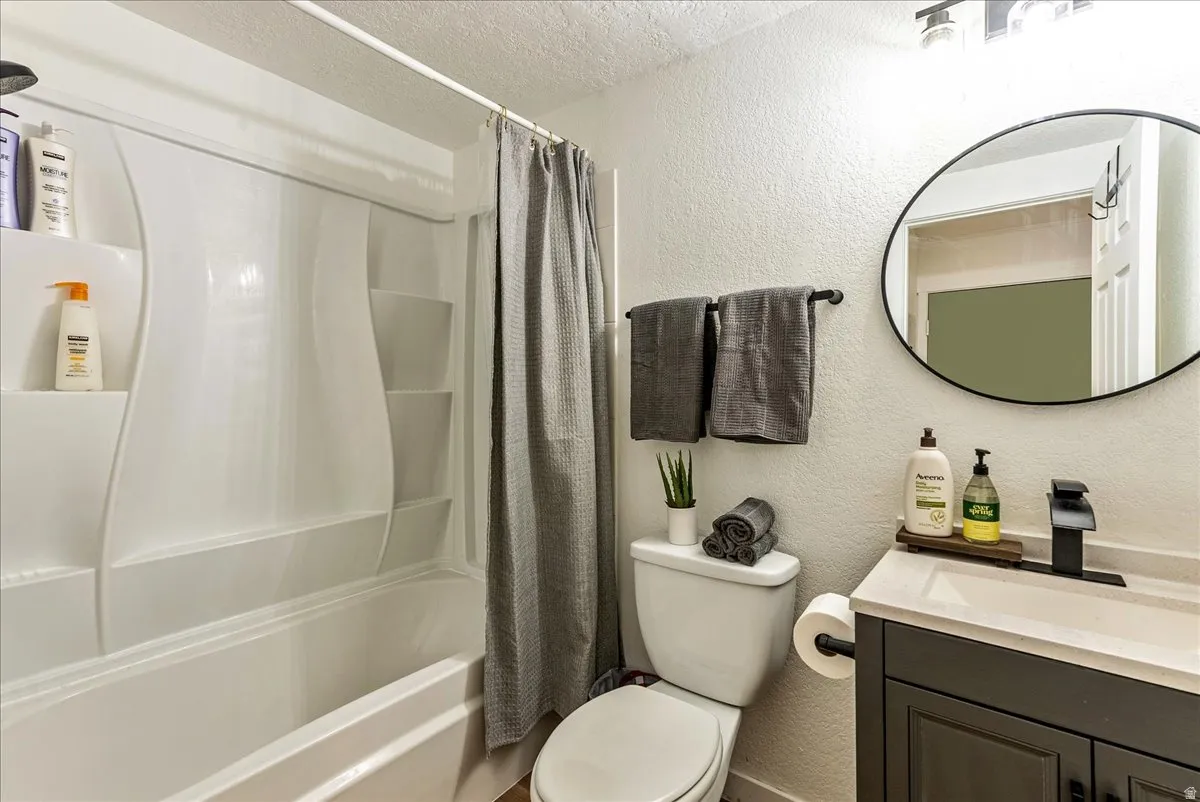 Bathroom featuring a white tub/shower combination, dark gray vanity with a single sink, black faucet, and a circular mirror
