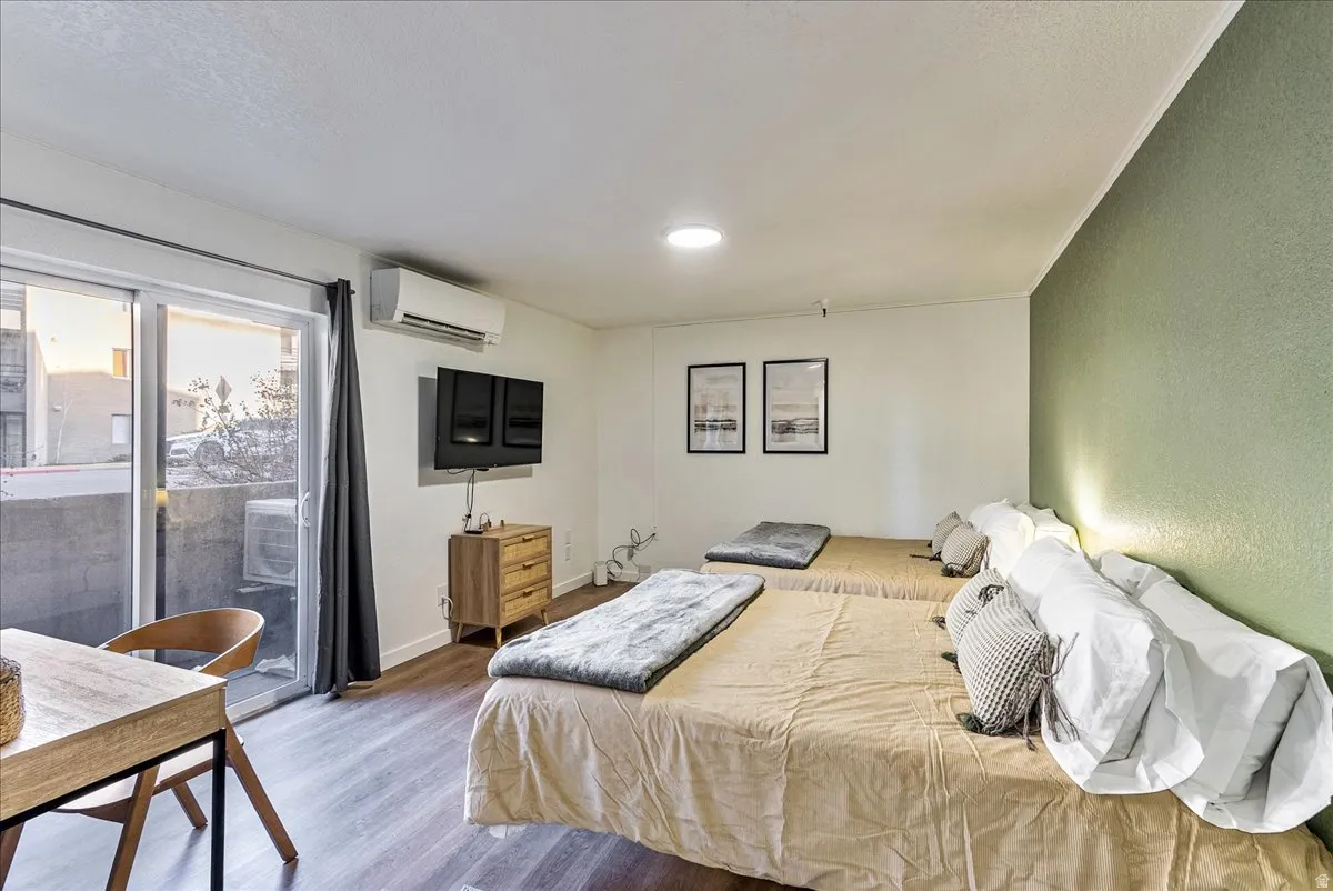Wood-finish flooring throughout this room featuring a sliding glass door leading to a balcony, a wall-mounted air conditioning unit, and a contrasting accent wall