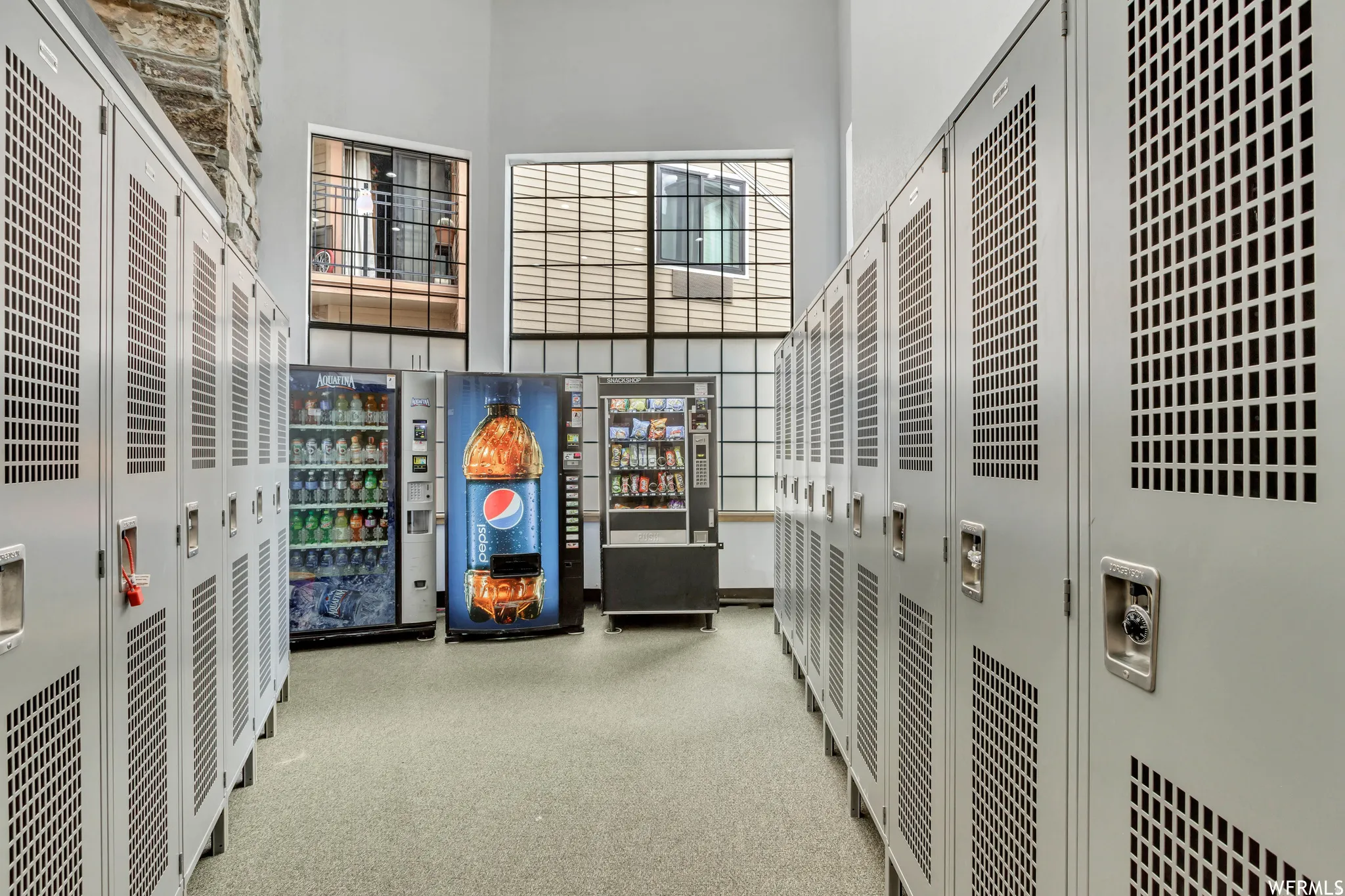 Corridor featuring rows of light gray lockers, high ceilings, and multiple windows