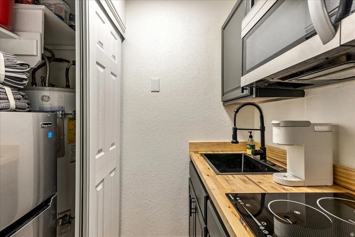 Compact kitchen area featuring wood-finish countertops, an undermount sink with a black gooseneck faucet, a built-in microwave, and an electric cooktop