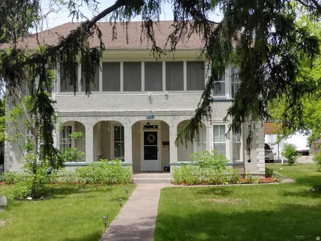 Two-story stucco residence featuring an arched portico, upper-level enclosed porch, a gabled roof, and a front walkway