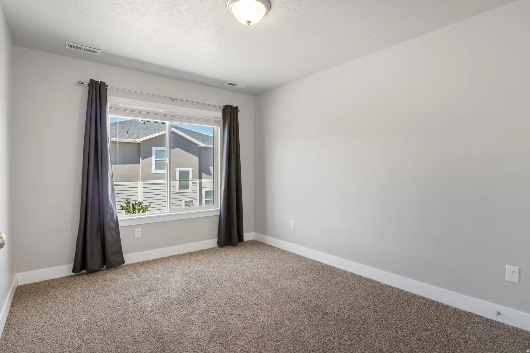 Carpeted room featuring a large window, neutral wall tones, white baseboards, and a semi-flush mount ceiling light fixture