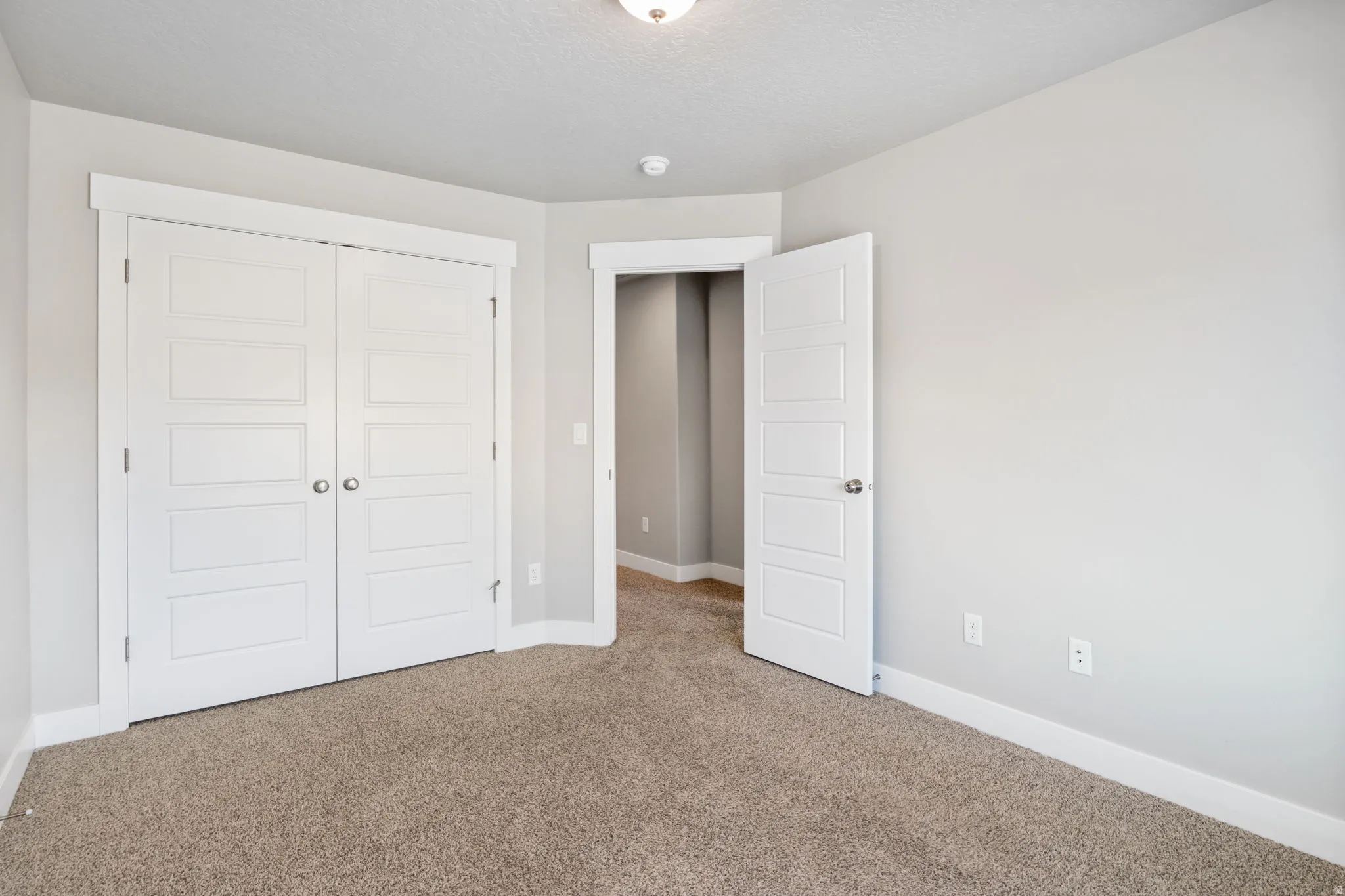 Neutral wall paint with textured carpeting, featuring a modern five-panel interior door and a bi-fold closet door with contemporary hardware