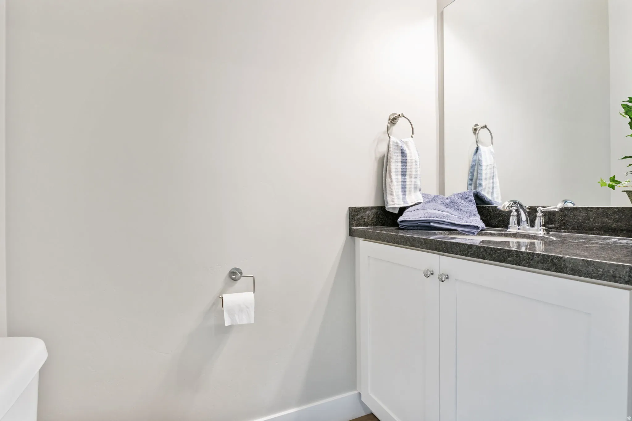 Bathroom vanity featuring a dark stone countertop, undermount sink, chrome faucet, and white cabinetry with silver-tone hardware